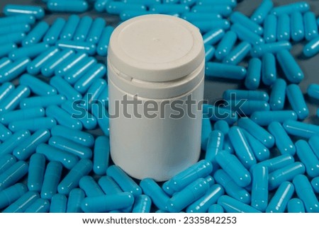 Blue antibiotic capsule pills texture with white bottle. Pharmaceutical production. Global health. Resistance to antibiotic drugs. Gelatin capsule pills, pharmaceutical industry.