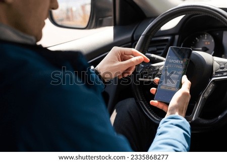 Close up cropped shot of man hand holding mobile phone with bookmakers website on its screen. Male gambler betting online using mobile application white sitting in a car.