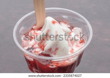 Strawberry Ice: A delectable ice cream treat served in a plastic cup, topped with luscious fruit syrup and filled with mouthwatering strawberry ice cream. Selective focus enhances the appeal.