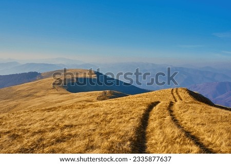 Mountain range with a dirt road among withered grass. Autumn mountain landscape in the Carpathian mountains