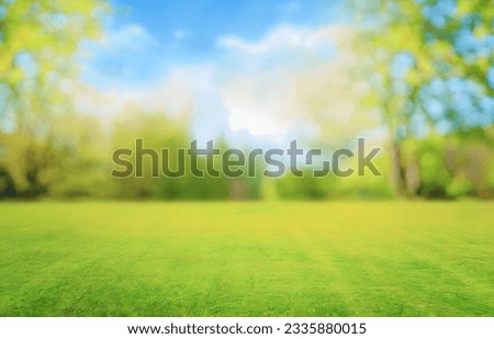 Beautiful blurred background image of spring nature with a neatly trimmed lawn surrounded by trees against a blue sky with clouds on a bright sunny day.

