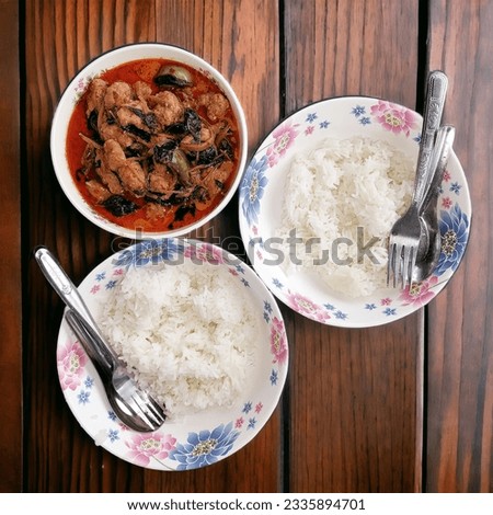 Picture of Thai food. There are 2 dishes of steamed rice and 1 red curry. Placed on an old wooden background.