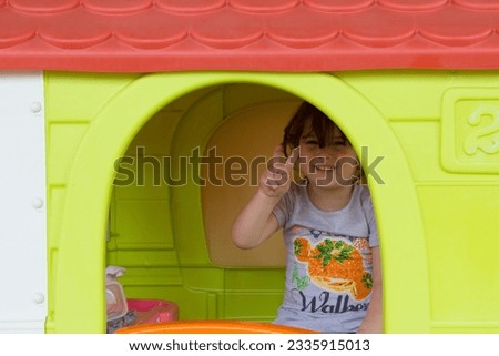Image of an adorable smiling little girl pointing her fingers to victory while playing in a playhouse in her home garden. Leisure and games for children
