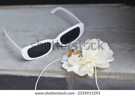 Sunglasses, white boutanier flower and newlyweds rings on a gray concrete surface. Wedding accessories.