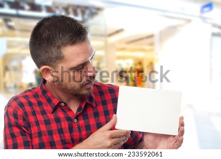 Man with red shirt over shopping center background. Holding a white card