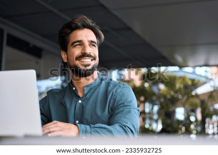 Happy young Latin business man using laptop computer sitting outdoor. Smiling Hispanic guy student or professional looking away in city cafe elearning, hybrid working, searching job online. Copy space