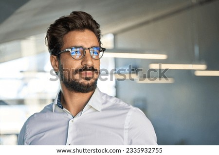Confident young Latin business man standing in office looking away, portrait. Hispanic businessman manager entrepreneur, male professional executive wearing eyeglasses thinking of investment market. Royalty-Free Stock Photo #2335932755