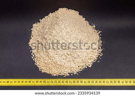 wheat, heap of wheat flakes next to measuring tape, black background, generated with extruder machine