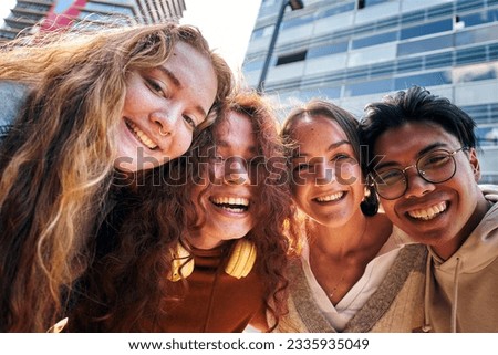 Group of friends taking selfie picture smiling looking at camera. Laughing young people celebrating standing outside and having fun. Portrait of four teens guys and girls enjoying in the city