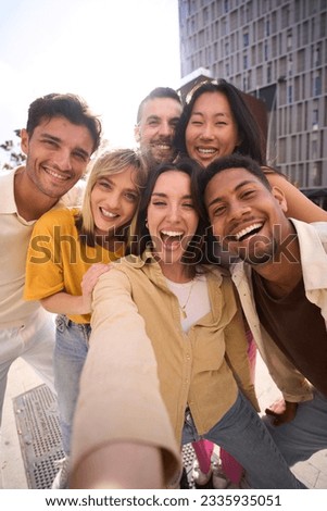 Vertical selfie of a Group of happy multiracial friends having fun outdoors at the park. Diverse cheerful joyful young people looking at the camera and smiling all together. They are hug and laugh