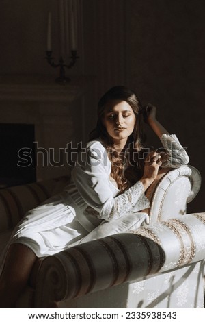 Portrait of a young attractive brunette with long hair in a white robe. She is sitting on a chair in the hotel. A dream bride.
