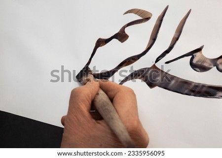 A calligrapher writing with pen and ink. man hands writing arabic calligraphy with ink. Arabic and Persian calligraphy. Written in Arabic, "In the name of God"