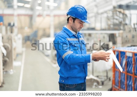 half body photo American male engineer Manager mechanic checking inventory in warehouse with listnote, holding radio, wearing helmet and uniform. In the plastic and steel industry
