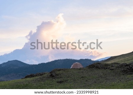 A hiker's tent on a green field overlooking beautiful mountain landscape. Tent on the mountain on the background of the sky with clouds in the background. Selective focus.