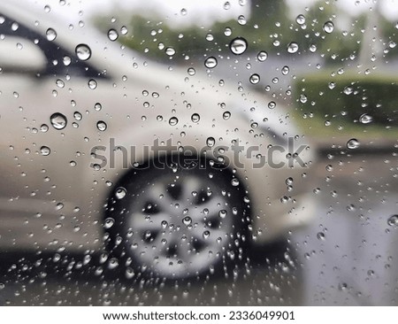 a photography of a car is seen through a rain covered window, view of a car through a rain covered window.
