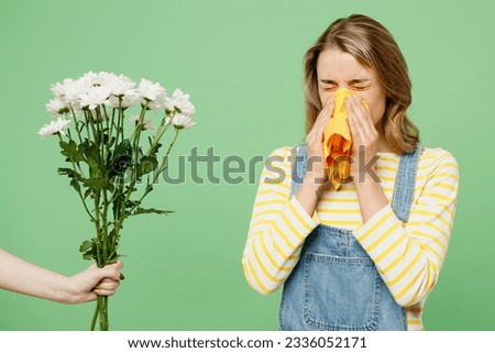 Sick unhealthy ill allergic woman has red watery eyes suffer from allergy trigger symptoms hay fever hold napkin flowers blow runny stuffy sore nose isolated on plain green background studio portrait Royalty-Free Stock Photo #2336052171