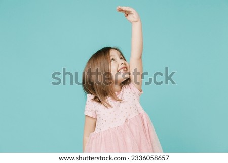 Little fun kid girl 5-6 years old wears pink dress hold hand above head show how much she grown try to be taller isolated on pastel blue color background child studio. Mother's Day love family concept Royalty-Free Stock Photo #2336058657