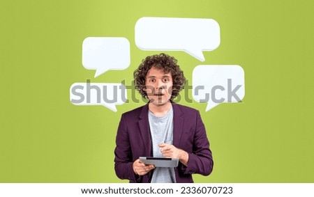 Surprised man finger pointing at tablet, looking at the camera with speech and thought bubbles mock up on green background. Concept of social media, online chat and news