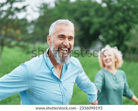 Happy active mid aged adult couple having fun walking running holding hands and bonding in park or nature outdoors
