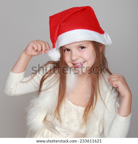 Studio image of a beautiful happy little girl in Santa's hat on a gray background for Christmas