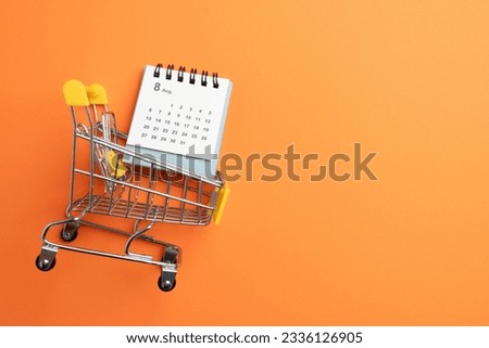 Shopping cart toy and calendar from the supermarket on table with orange background, Sale buy mall market shop consumer concept. Copy space