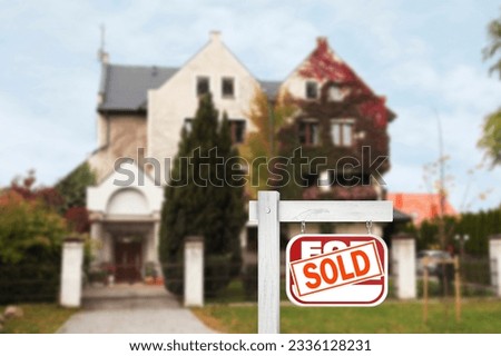 Red sale sign with Sold sticker near house