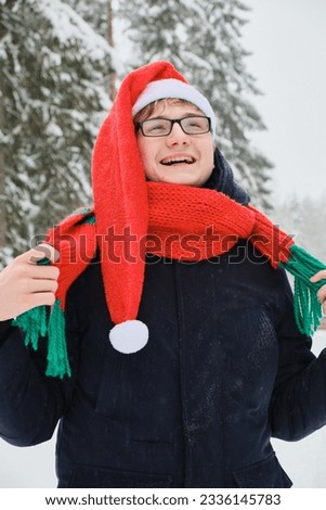 portrait of a young guy in glasses in winter, a red santa hat and a knitted warm scarf, winter snowy weather outside, christmas mood concept
