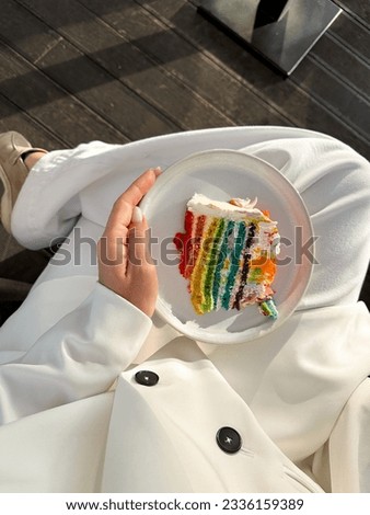 Aesthetic summer postcard picture. Vertical format. Lady in white suit is holding a plate with a piece of rainbow cake