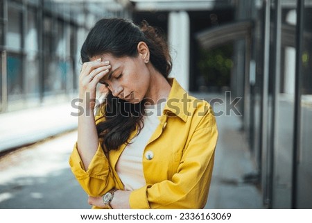 Painful girl suffering migraine touching temple in the street. Front view portrait of a dizzy young woman feeling sick on a city street. Single woman suffering headache walking on the street