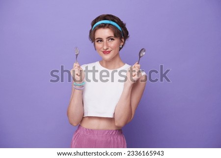 Portrait beautiful smiling young hungry woman holding spoon and fork isolated on purple background. Royalty-Free Stock Photo #2336165943