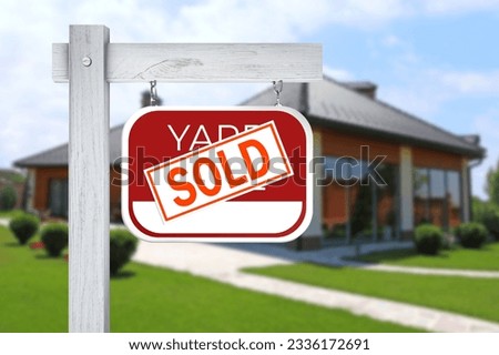 Yard sale sign with Sold sticker near house