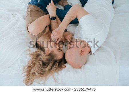Top view on couple in love laying on bed looking at each other. Young caucasian blonde woman touching husband at bedroom. Bald man enjoying weekend with wife at hotel on vacation, honey moon. Royalty-Free Stock Photo #2336179495