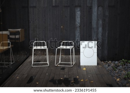 A white chair stands on a wooden floor, with a black backdrop made of wood burning fire, giving it a unique pattern.