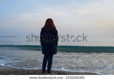 A lonely woman watches the sea. It can be used in studies with the theme of loneliness, solitude, sadness. Royalty-Free Stock Photo #2336206383