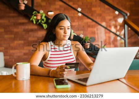 Attractive hispanic woman in her 20s paying with her credit card while online shopping on her laptop