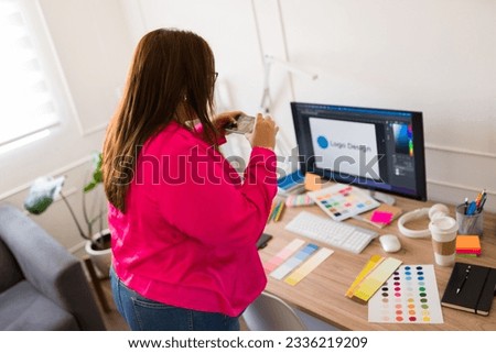Professional woman working as a graphic designer taking pictures of the color swatches on her office desk 