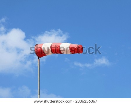 Windsock indicator of wind. Horizontally flying windsock ( wind vane ) with blue sky and white clouds in  the background. Wind cone indicating wind and force. Royalty-Free Stock Photo #2336256367