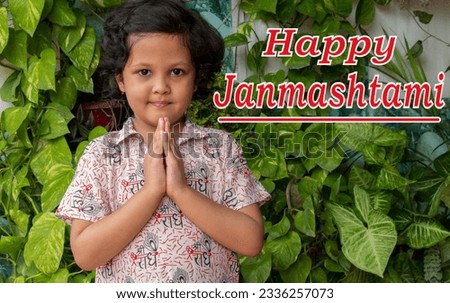 Happy Janmashtami means birthday of hindu god Krishna text  word greeting written. Indian girl smile and holding palms together in Namaste gesture on an outdoor in plant and garden background.