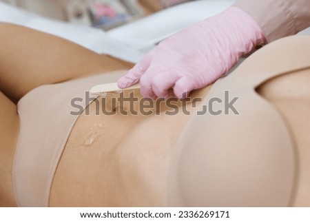 Bikini laser epilation and cosmetology. Hair removal cosmetology procedure. Woman wearing protective gloves applying gel on woman's bikini area to prepare for laser depilation.