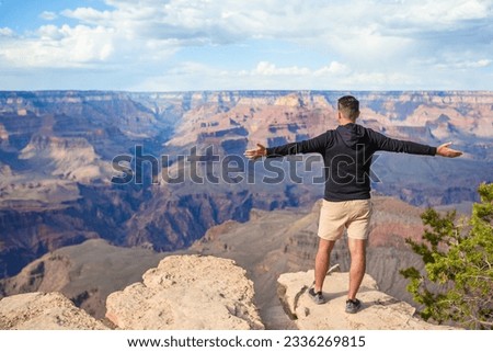 Young hiker standing on a steep cliff taking in the amazing view over famous Grand Canyon on beautiful sunny day in summer, Grand Canyon National Park, Arizona. High quality photo