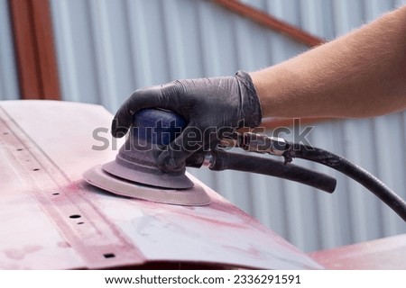 A man working with grinding tool. Sanding of car elements. Hands in black gloves hold a power tool. Removing paint from a car element. Close up. Royalty-Free Stock Photo #2336291591