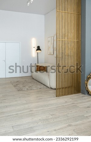 a soft comfortable sofa with a floor lamp is an open-plan apartment in a modern style with light walls and wooden floors and a stylish golden partition Royalty-Free Stock Photo #2336292199