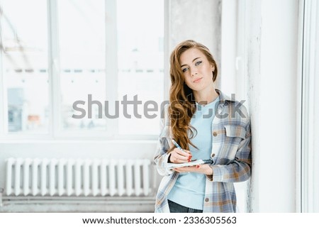 Young beautiful long haired college student girl in casual shirt with notebook, pen. Businesswoman making notes in organizer. Content portrait photo shoot for advertising in social networks, website.