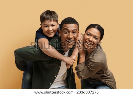 Portrait of happy cheerful black family father, mother and school aged cute son posing together on beige colored studio background, parents and child enjoy time together. Love, affection, parenthood