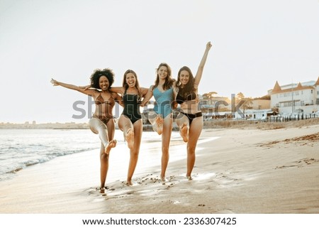 Four happy ladies having good time at the beach, embracing while walking on coastline, young women laughing and enjoying their vacation by the ocean