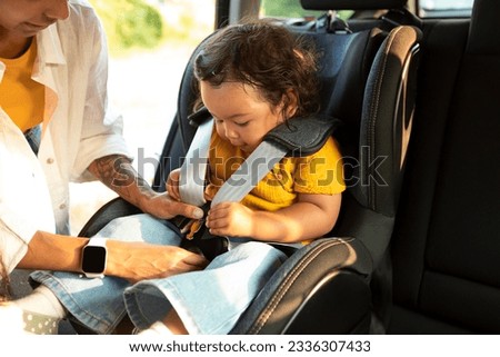 Asian Mom Sitting Down Her Toddler Daughter In Baby Car Seat, Adjusting Harness Straps For Safety During Automobile Journey. Cropped Shot, Closeup Of Child In Chair For Safe Auto Trip Royalty-Free Stock Photo #2336307433