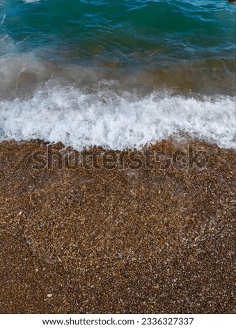 Beautiful sea background with pebble beach and blue waves with sea foam.