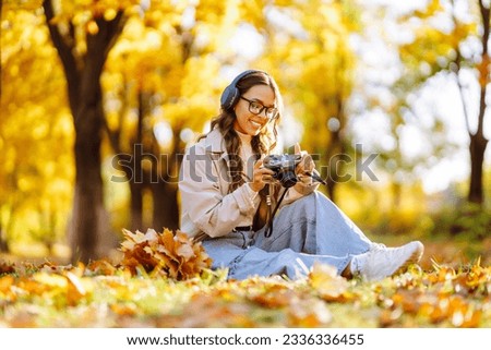 Beautiful woman taking pictures in the autumn forest. Smiling woman enjoying autumn weather. Rest, relaxation, tourism, lifestyle concept.