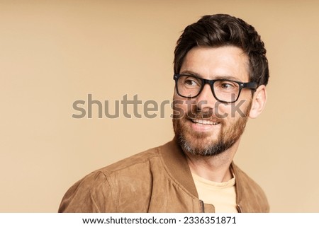 Portrait of smiling handsome bearded man wearing stylish eyeglasses looking away isolated on beige background, copy space. Vision concept  Royalty-Free Stock Photo #2336351871