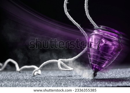 Closeup of a toy top spinning in a grey textured surface and a black background. Royalty-Free Stock Photo #2336355385